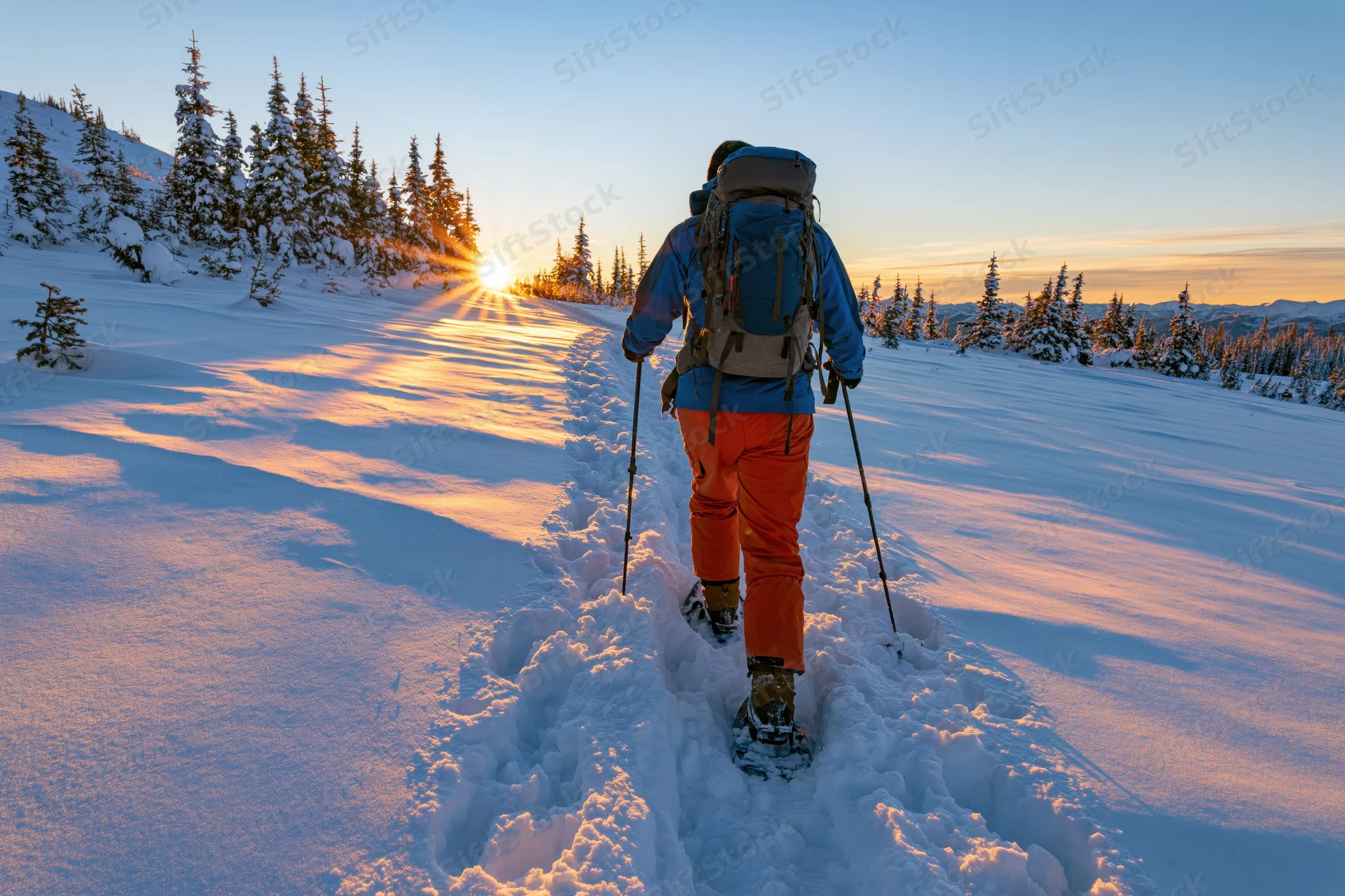 Snowshoer walking on snowy trail toward sunrise in mountain forest