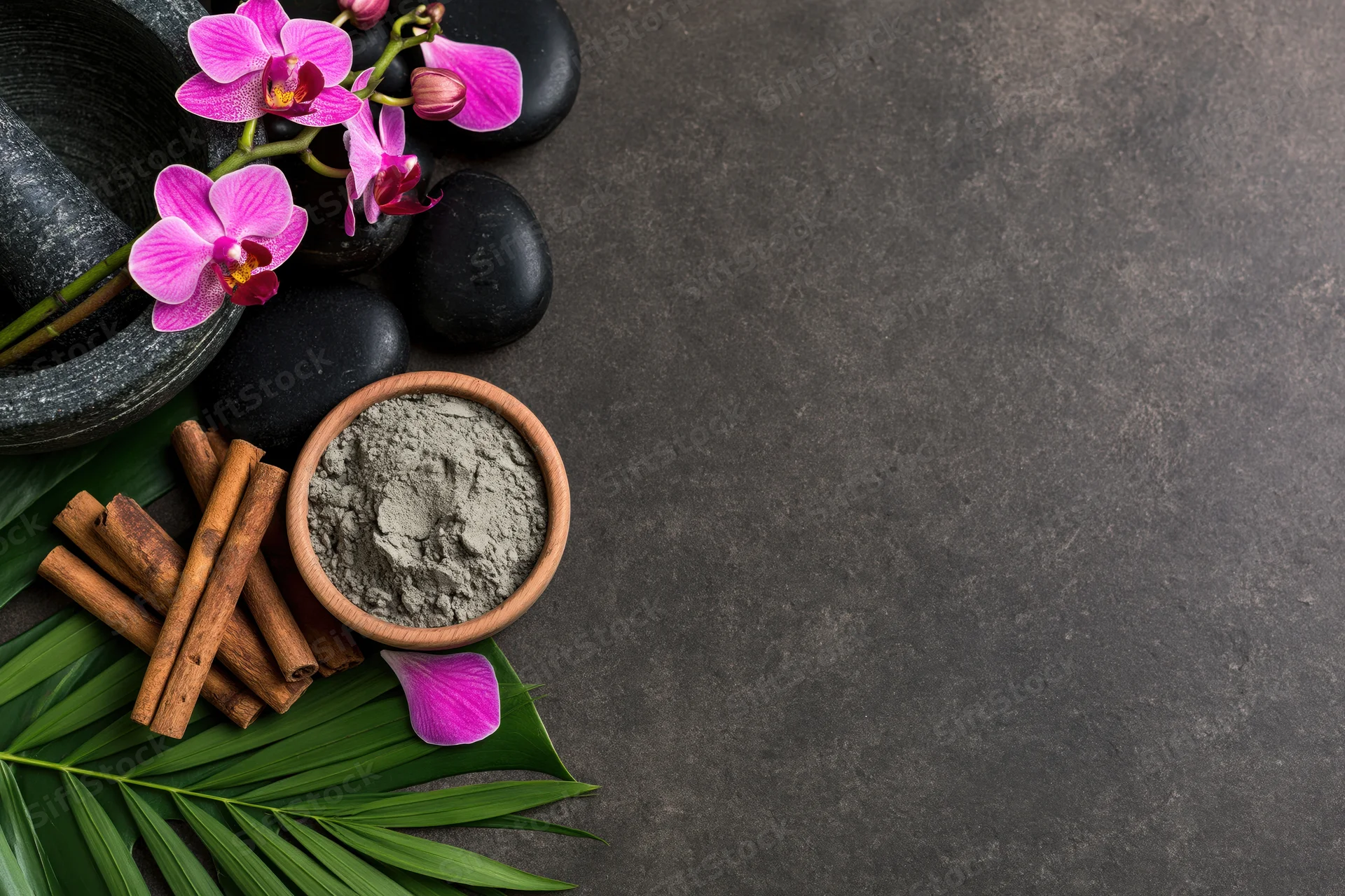 Spa arrangement with orchids, cinnamon sticks, and gray powder on dark slate surface