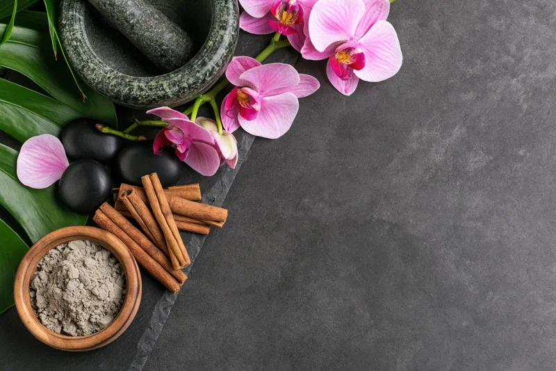 Spa arrangement with orchids, cinnamon sticks, mortar and pestle, and powder on dark slate surface