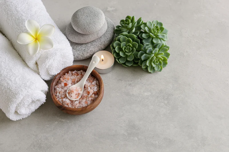 Spa flat lay with towels, stones, candle, succulents, and bath salt on a grey surface