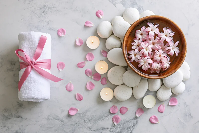 Spa flat lay with rolled towel, floating jasmine flowers, smooth stones and lit candles on marble surface