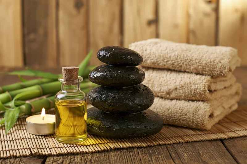 Stacked basalt stones and essential oil bottle on bamboo mat with towels and candle in spa setting