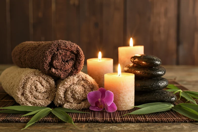 Rolled towels and lit candles arranged with smooth stones and orchid on bamboo mat