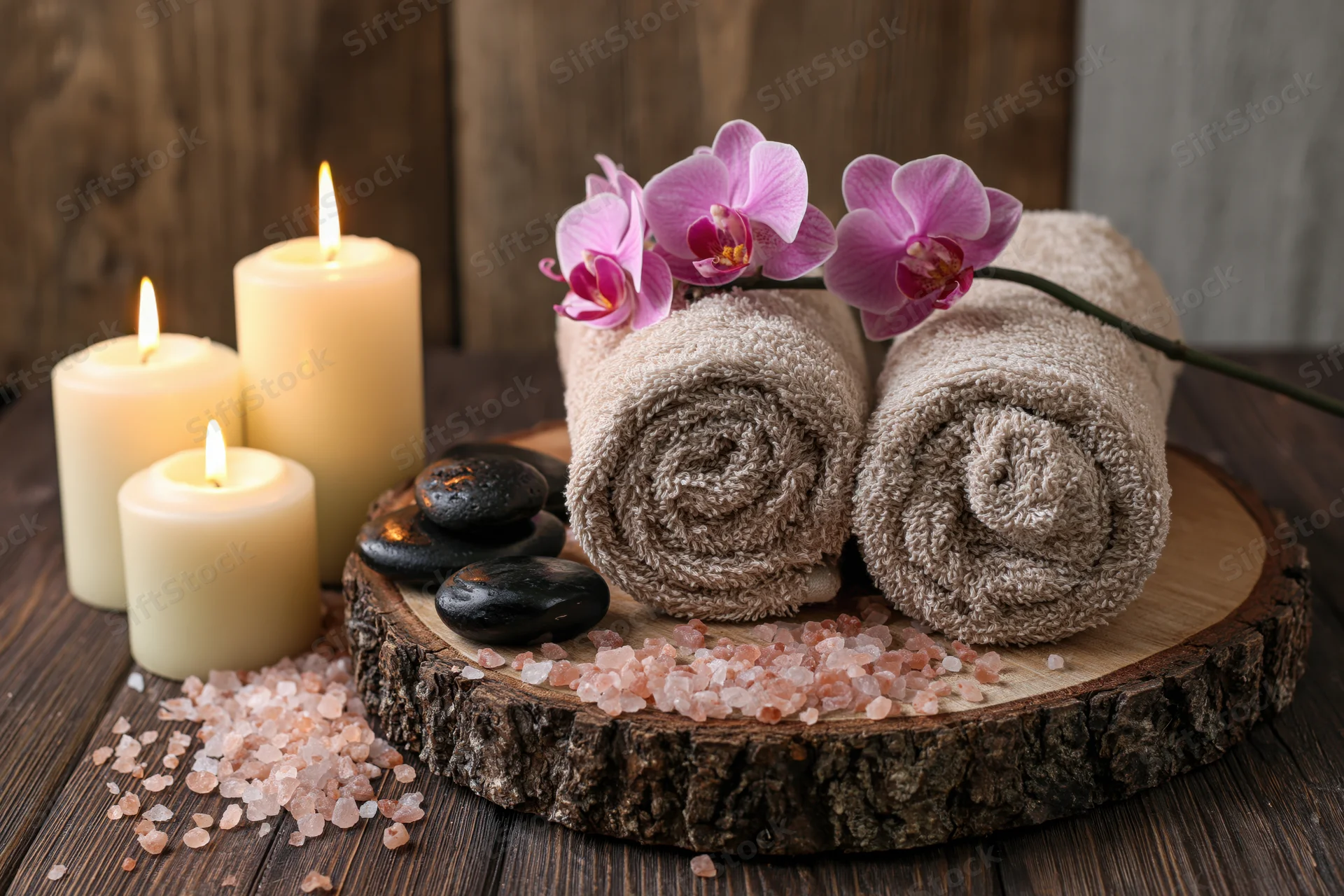 Rolled towels and orchid on wooden tray with candles and salt stones for spa relaxation