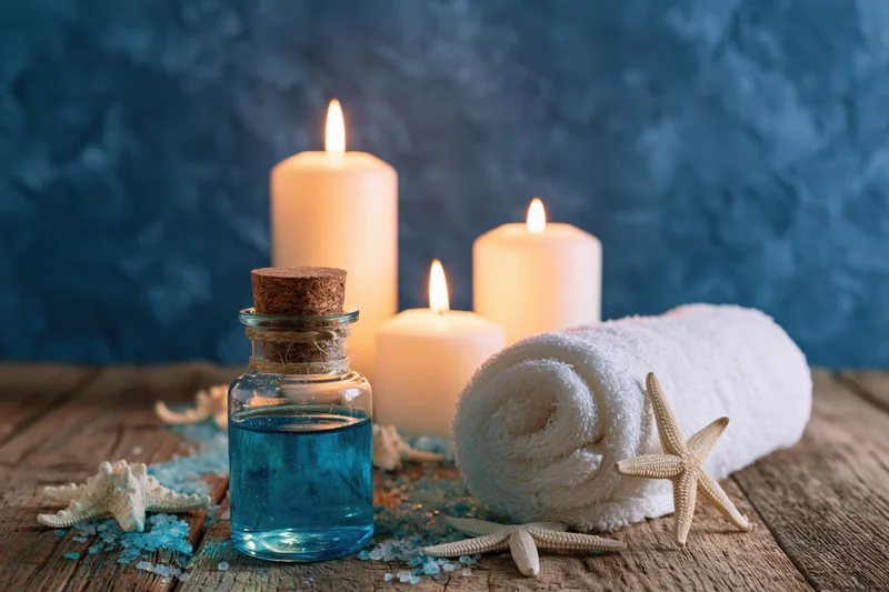 Spa still life with lit candles, rolled towel, starfish, and blue essential oil bottle on rustic wooden surface