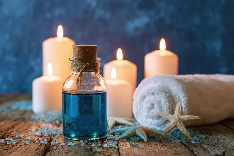 Blue essential oil bottle with lit candles, towel and starfish on rustic wood surface