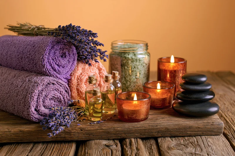 Rolled towels, lavender, candles and stones arranged on a rustic wooden surface for spa still life