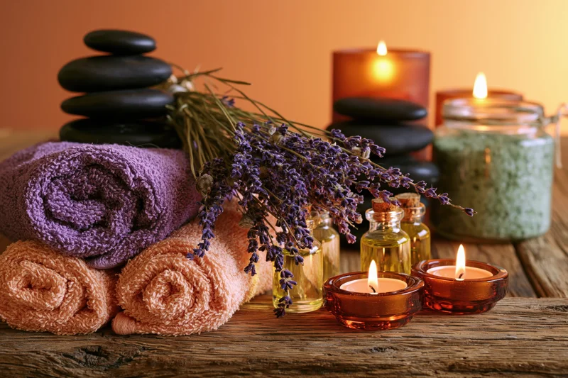 Rolled towels, lavender, candles and stones arranged on a rustic wooden surface for spa relaxation