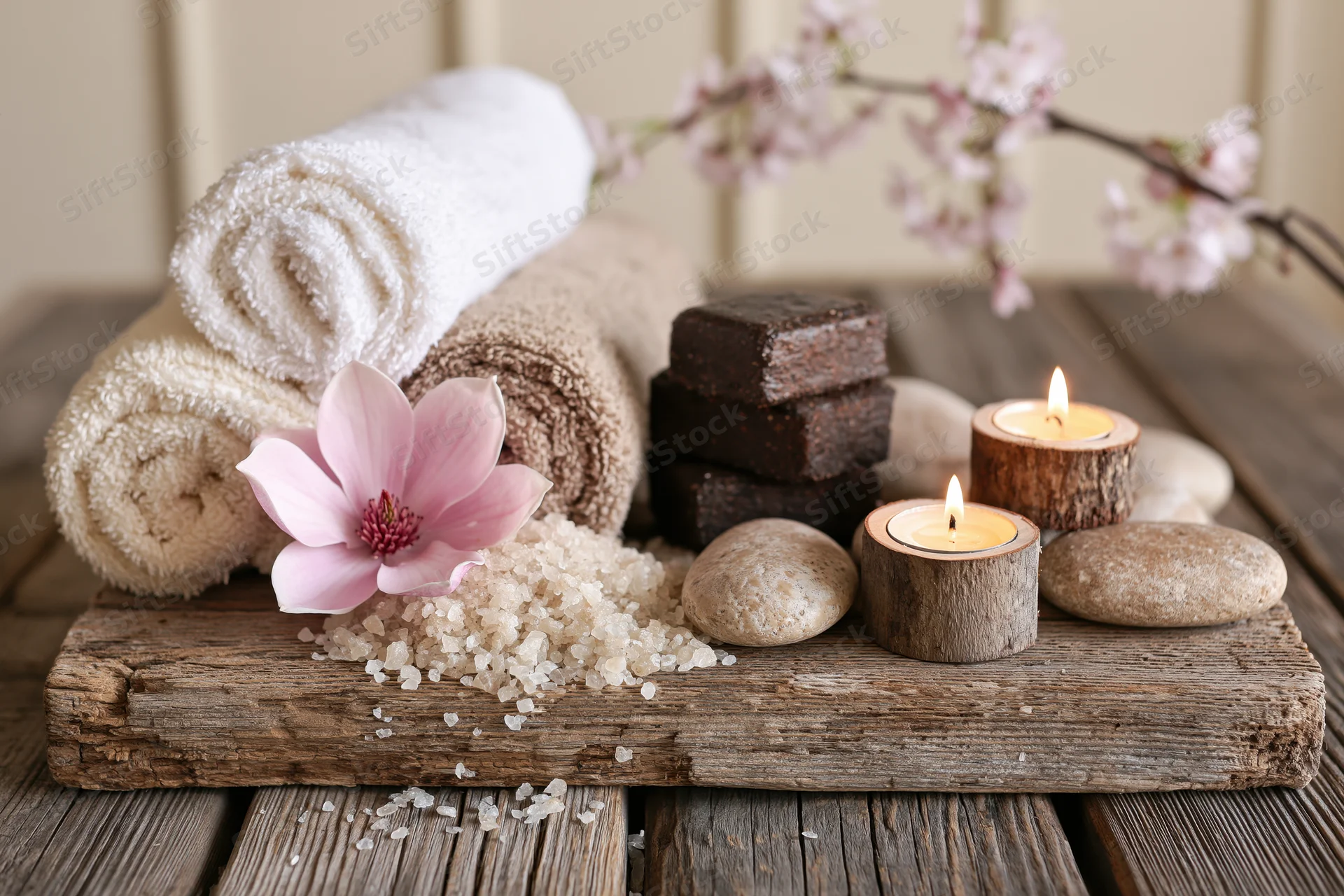 Spa still life with candles, towels, stones and flowers on a weathered wooden plank