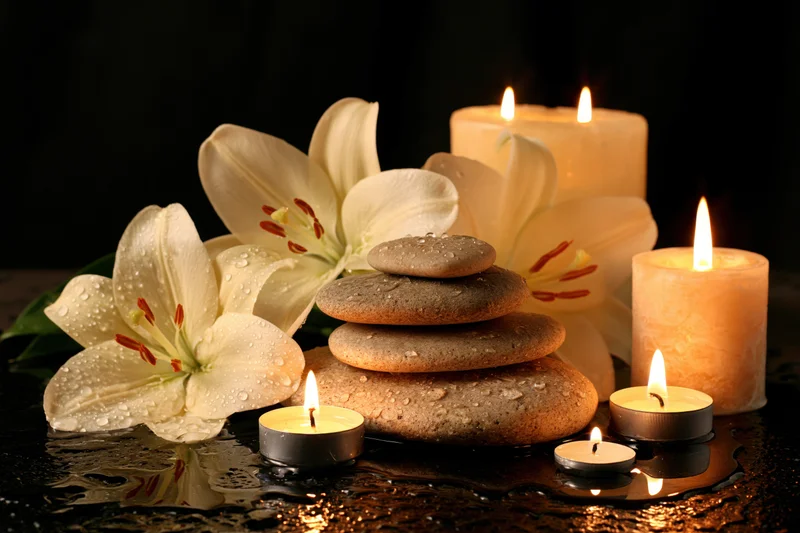 White lilies and smooth stones arranged with lit candles on a wet black surface