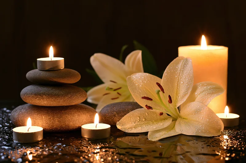 White lily flowers and stacked stones with lit candles on wet reflective surface in dim spa setting