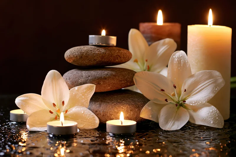 White lily flowers and lit candles arranged with smooth stones on a dark reflective surface