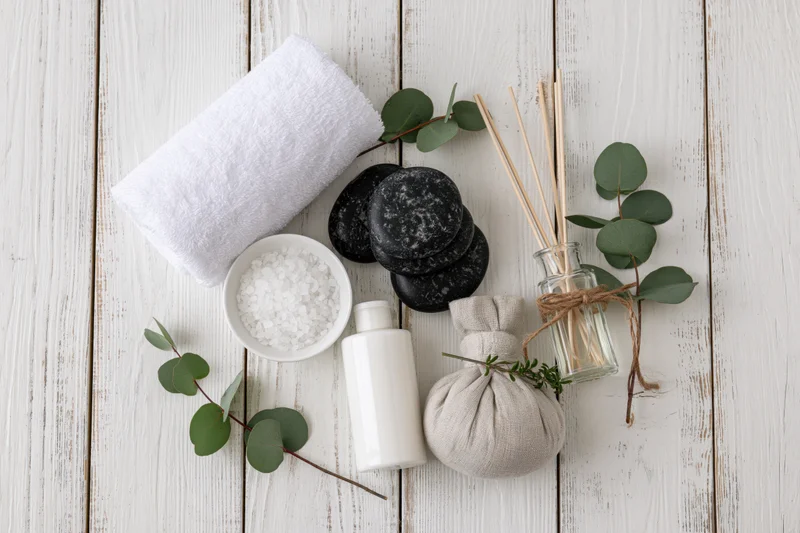 Spa wellness products arranged in flat lay on white wooden surface with eucalyptus and stones