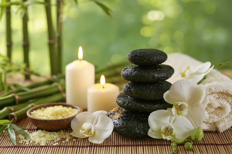 Spa still life with stacked stones, lit candles, white orchids, and rice on a bamboo mat