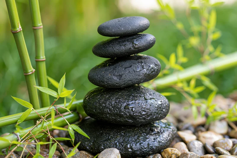 Stack of smooth black basalt stones balanced in a garden with bamboo and green foliage