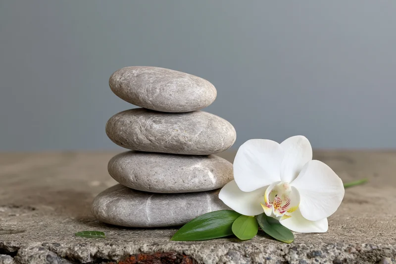 Stack of smooth grey zen stones balanced beside a white orchid on a worn concrete surface