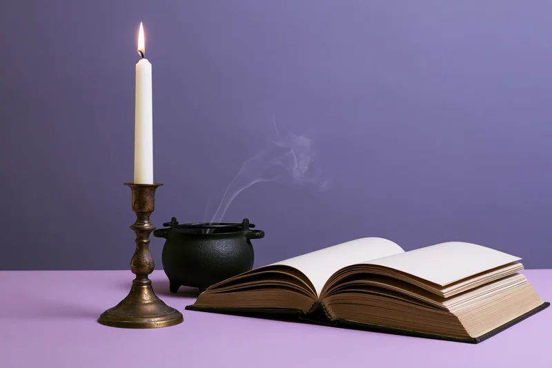Open book beside lit candle and smoking cauldron on purple surface
