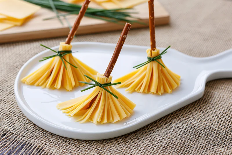 Three cheese and pretzel witch broom appetizers arranged on a white plate on burlap fabric