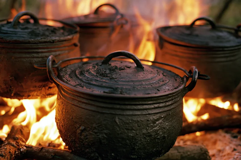 Blackened cast iron potjie pots with lids cooking over an open campfire
