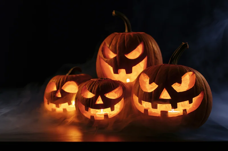 Four carved pumpkins glowing with candles in a smoky dark setting