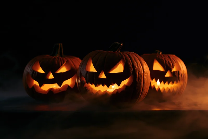 Three carved pumpkins glowing with candles inside on a dark smoky surface