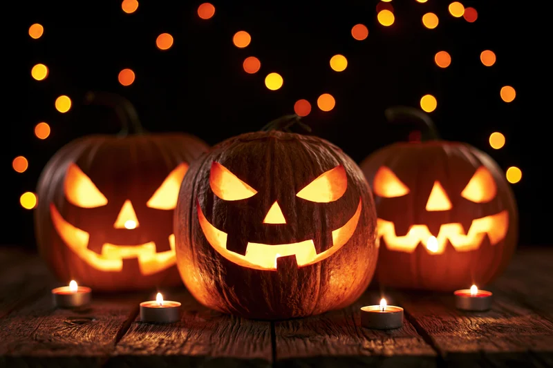 Three carved jack-o-lanterns glowing with candles on a wooden table at night
