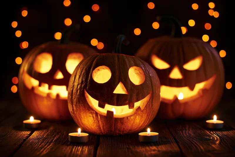 Three carved jack-o-lanterns glowing with candles on a wooden table at night