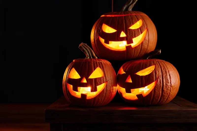 Three carved pumpkins glowing with light arranged on a wooden table