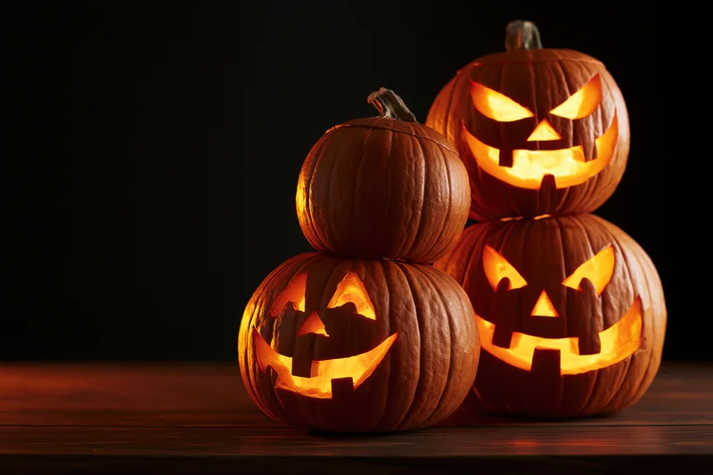 Three carved jack-o-lanterns glowing on a wooden table against a dark background