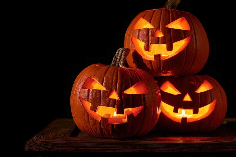 Three carved pumpkins glowing with candles on a wooden table against a dark background