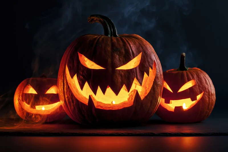 Three carved jack-o-lanterns glowing with candles on a dark surface