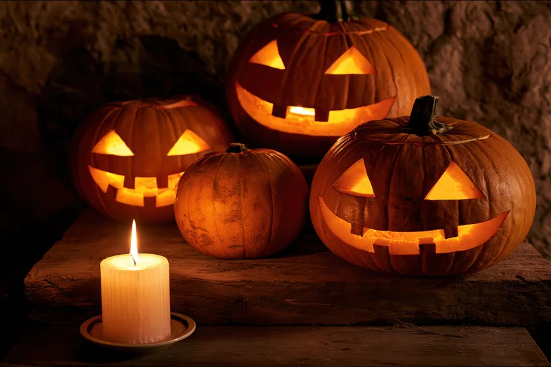 Three carved jack-o-lanterns glowing with candlelight on a wooden table against a stone wall