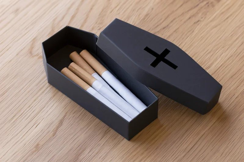 Cigarettes inside a miniature black coffin-shaped box on a wooden surface