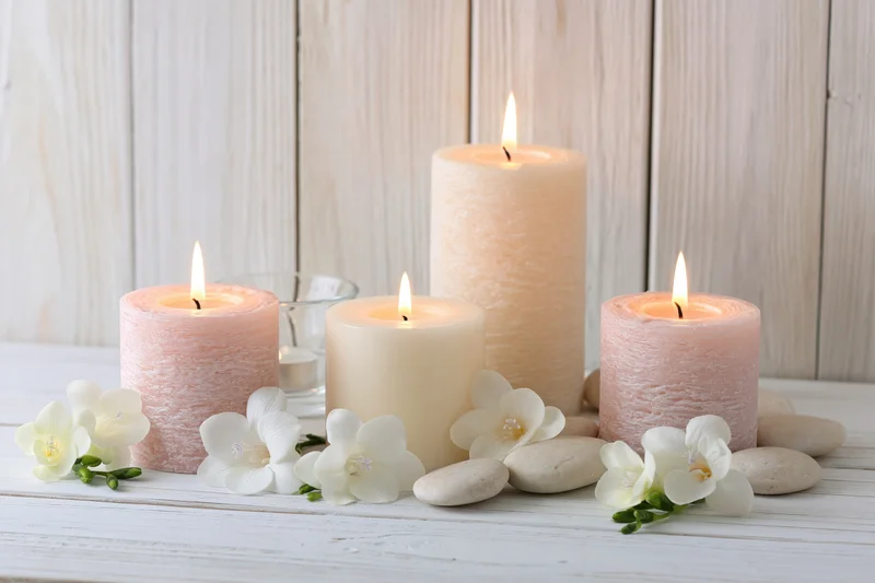 Lit pillar candles in soft blush and cream tones arranged with white orchids and smooth stones on a white wooden table