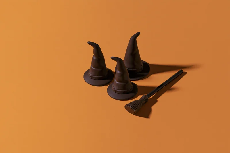 Three small dark witch hats and a miniature broomstick arranged on an orange surface