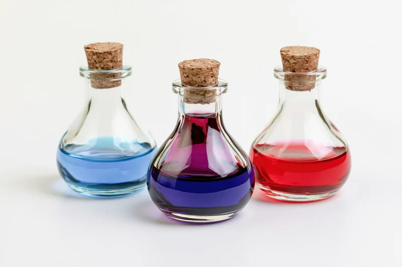 Three small glass bottles with cork stoppers containing colored liquids arranged in a row on a white surface