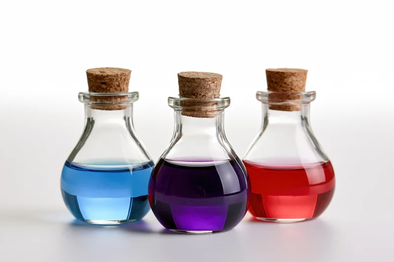 Three small glass potion bottles with cork stoppers filled with blue, purple, and red liquids arranged in a row on a white surface