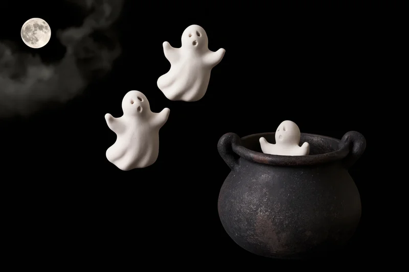 Three white ceramic ghost figurines floating near a black cauldron against a dark night sky with a full moon