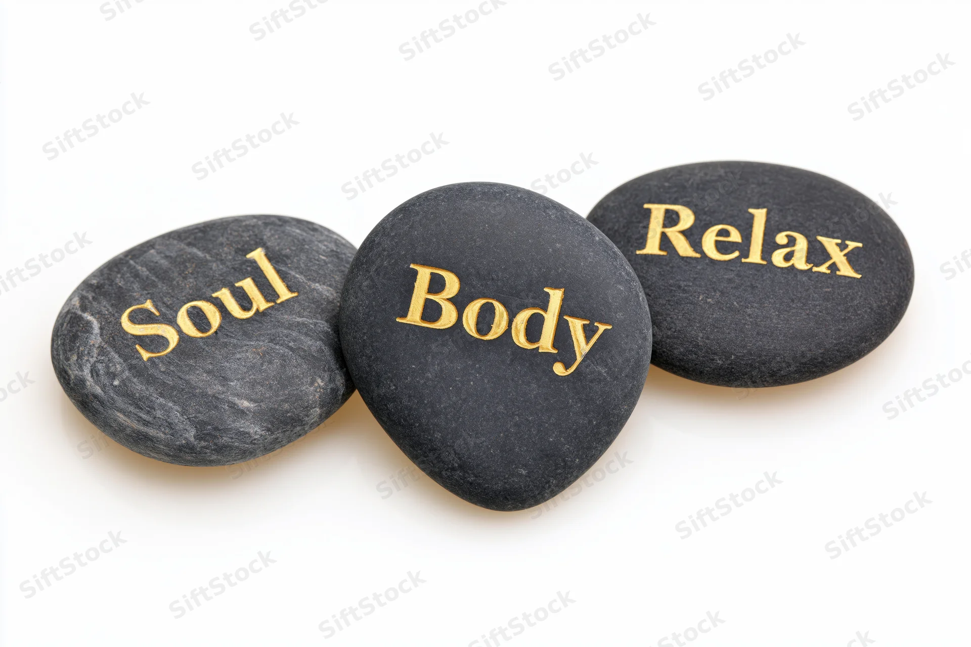 Three dark smooth basalt spa stones engraved with gold words soul body relax arranged diagonally on white background