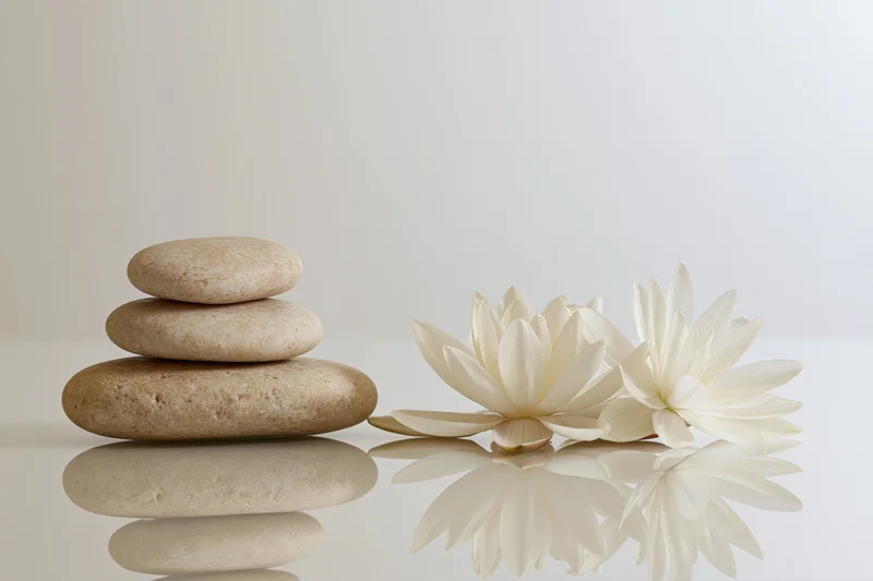 Stacked smooth stones beside white lotus flowers on reflective surface