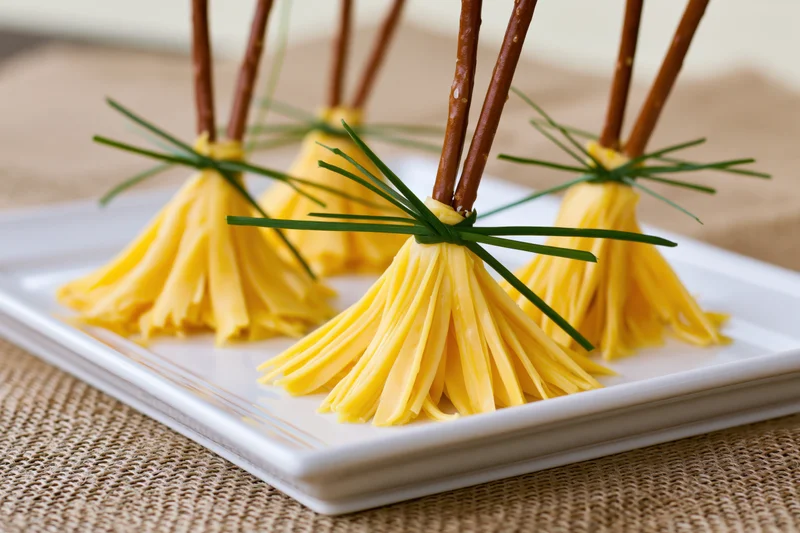 Witch broom appetizers made from sliced yellow cheese and pretzel sticks on a white plate