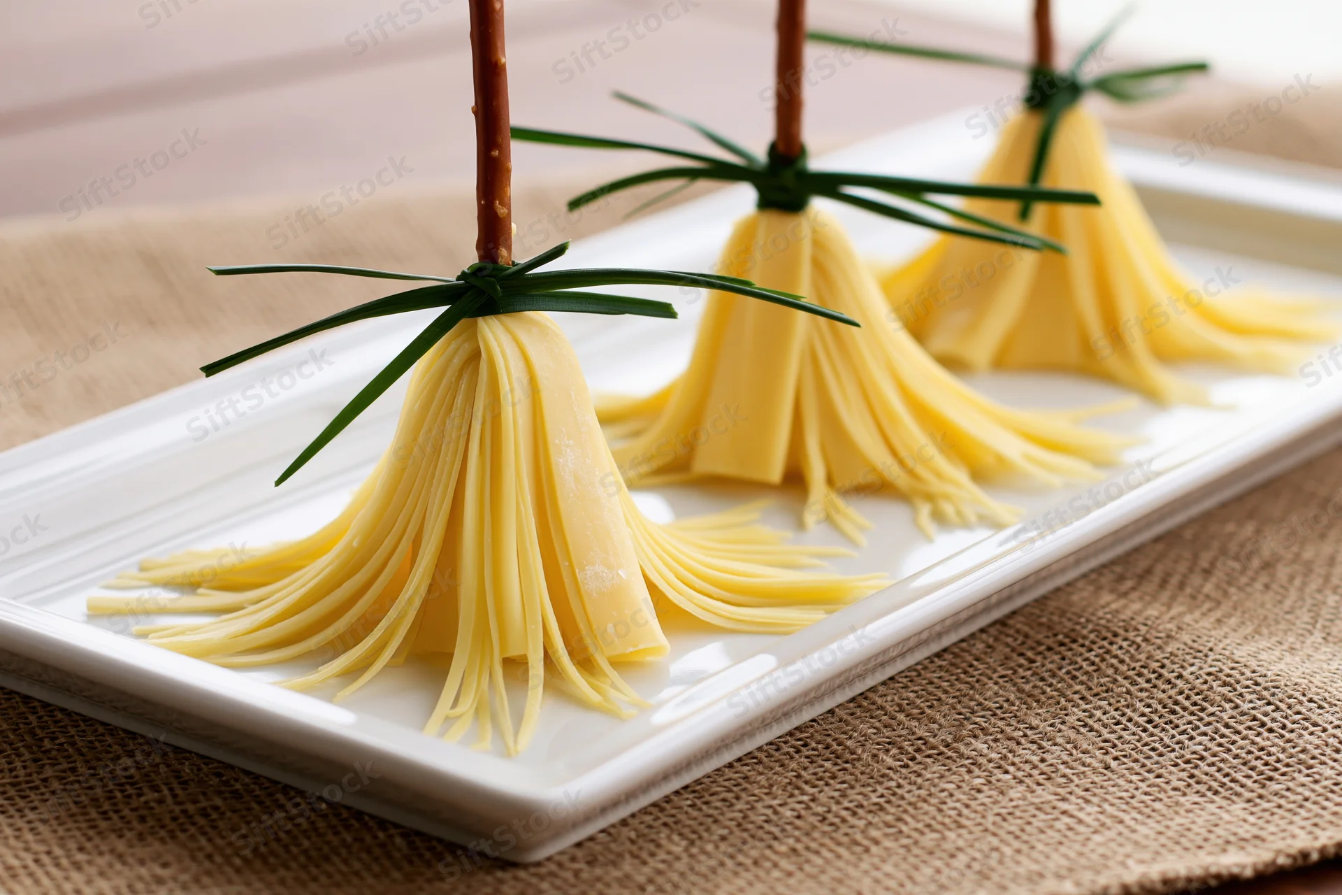Three cheese broom appetizers arranged on a white rectangular plate on burlap fabric