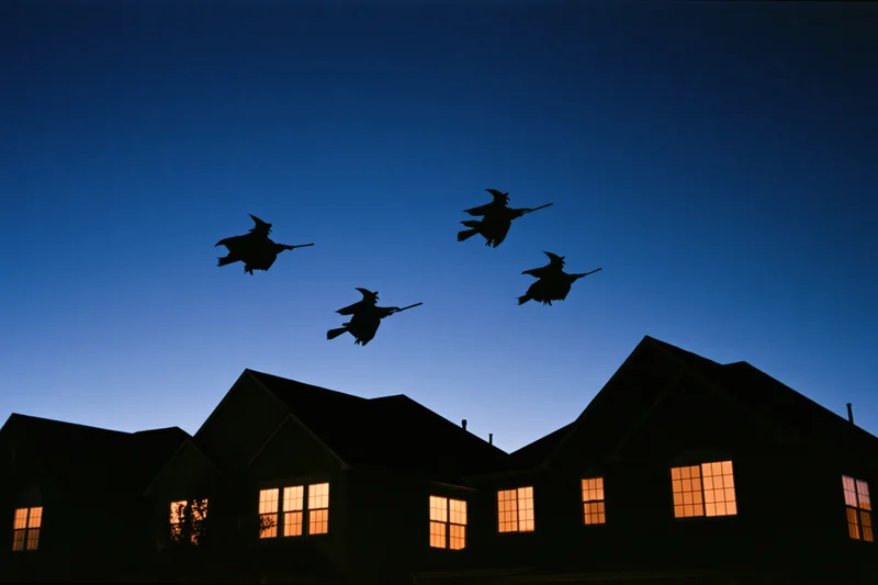 Silhouettes of witches flying on broomsticks over suburban houses at twilight