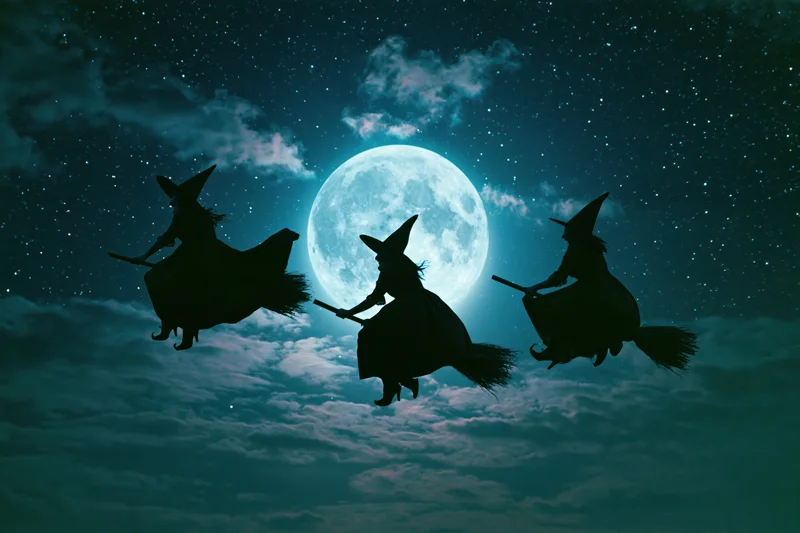 Three witches flying on broomsticks across a full moon at night