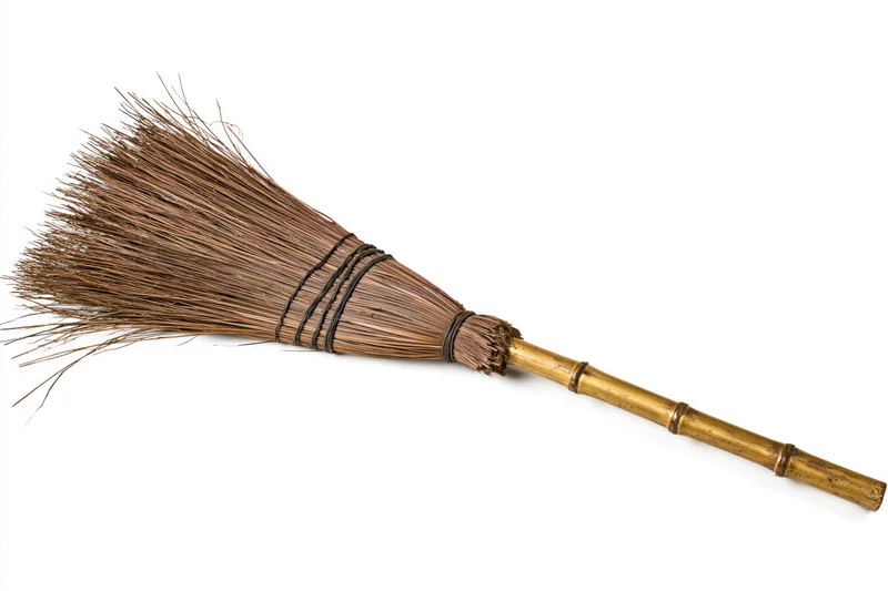 Traditional straw broom with worn bamboo handle lying on white background