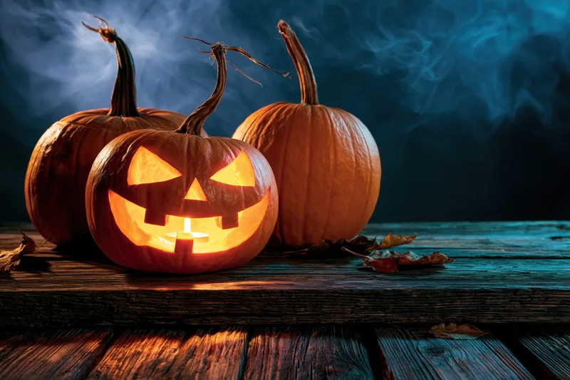 Carved pumpkin glowing with candlelight on weathered wooden surface with smoke and autumn leaves