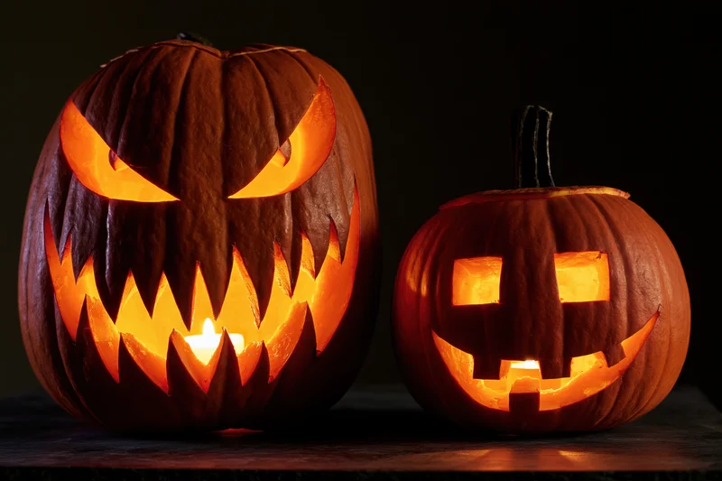 Two carved pumpkins with glowing faces side by side on a dark surface