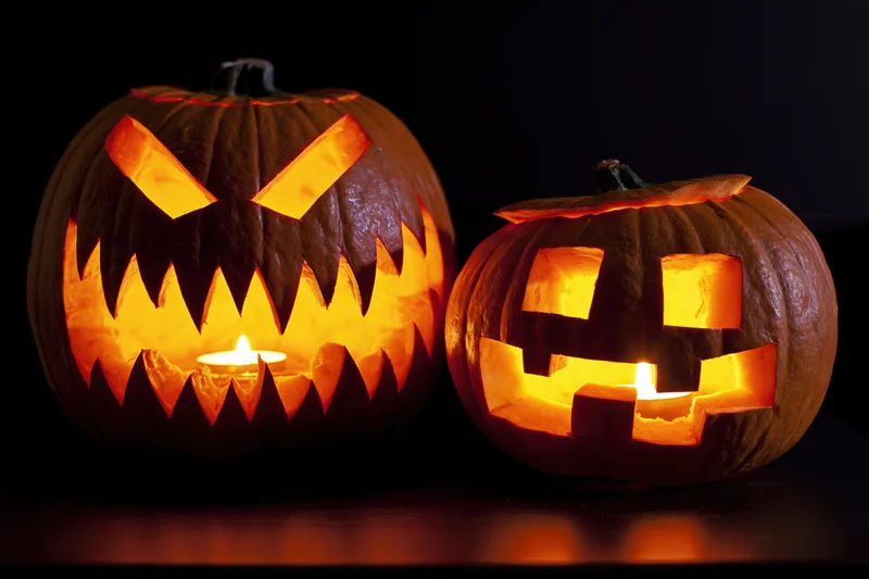 Two carved pumpkins with lit candles side by side on a dark surface