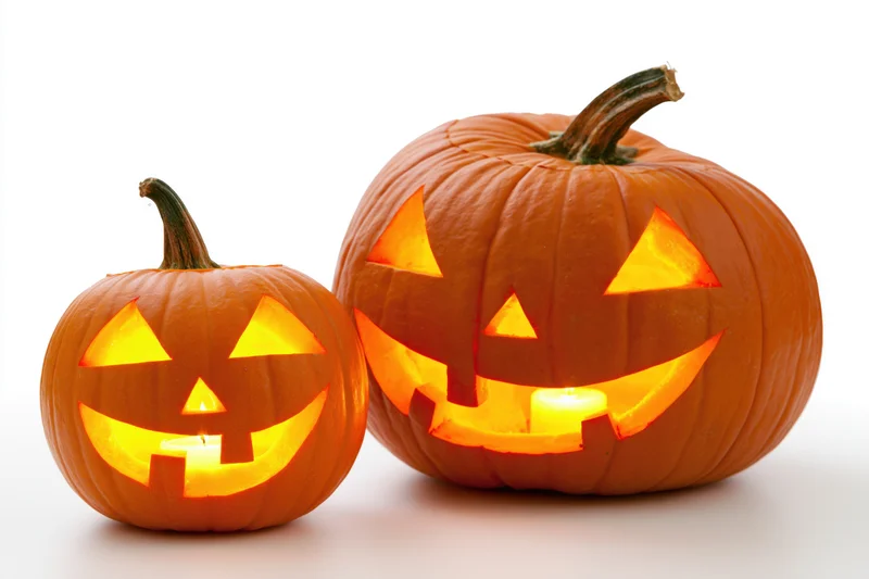 Two carved pumpkins glowing with candles on a white surface