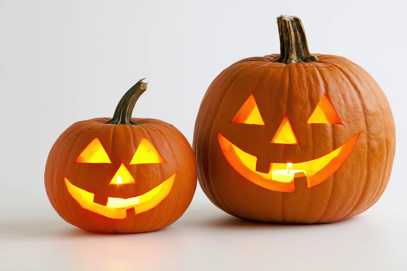 Two carved pumpkins with glowing faces side by side on white background